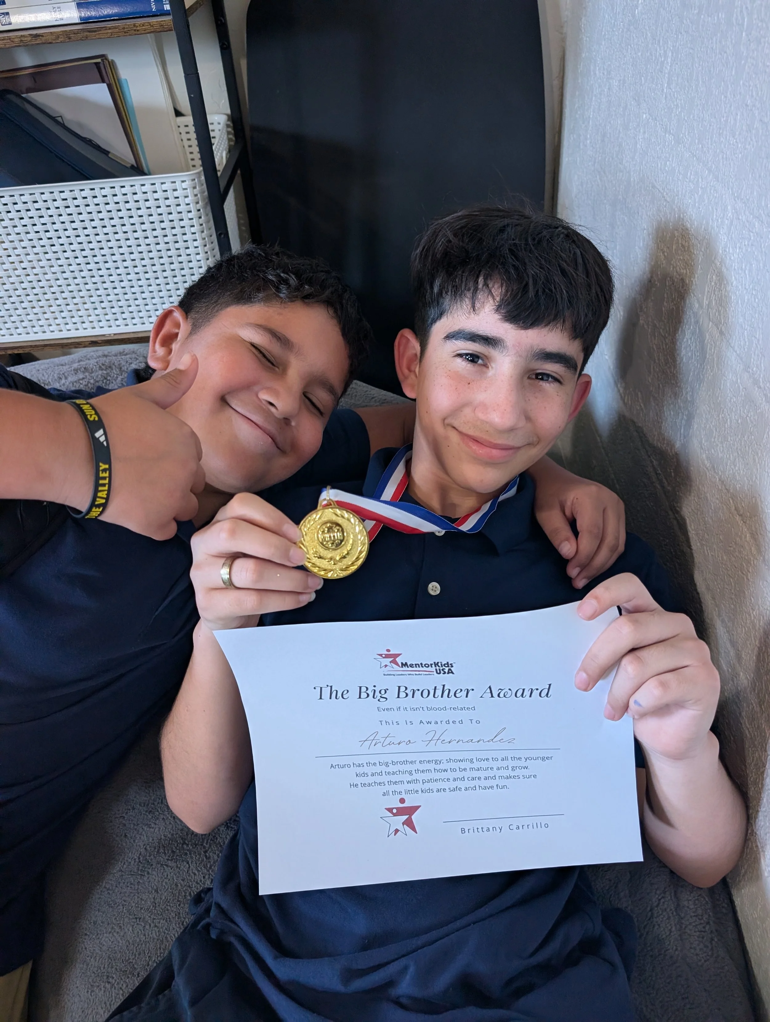 Two MentorKids students smile together as one holds a gold medal and a Big Brother Award certificate.