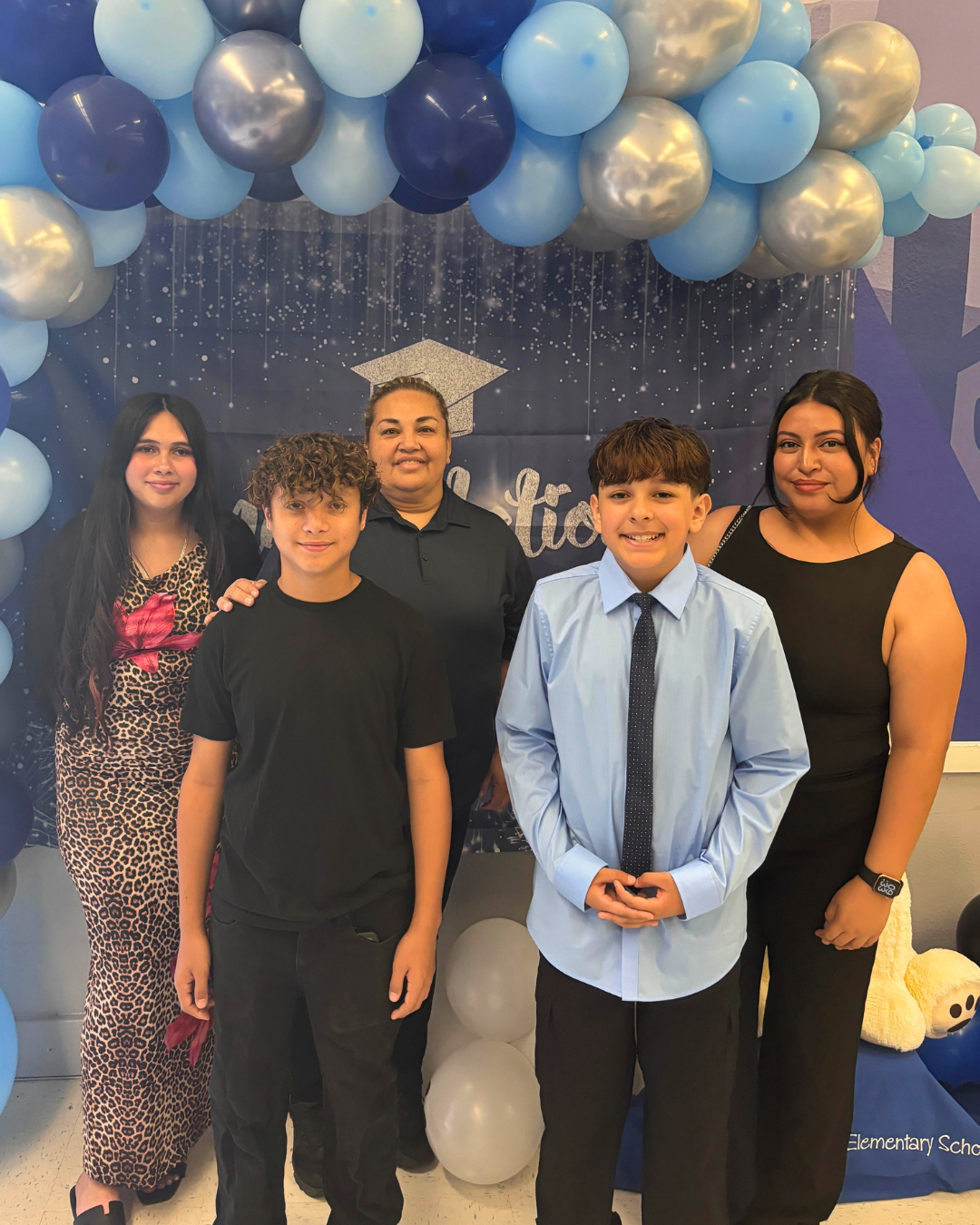 Two young people and three adults pose beneath blue and silver balloons at a Maryvale school celebration.
