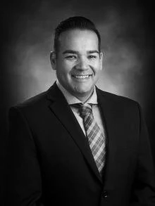 Portrait of a man in a suit smiling against a brown background.