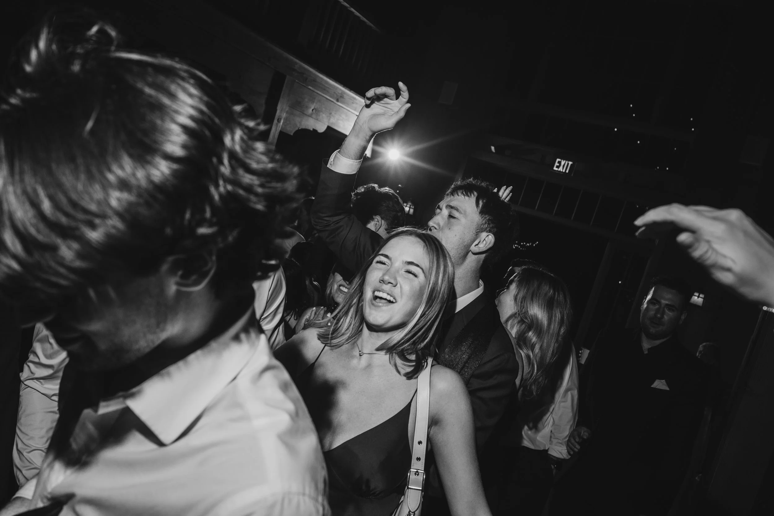 A lively group of young adults at a party, dancing and enjoying themselves, indoors with a dark background and bright lights.