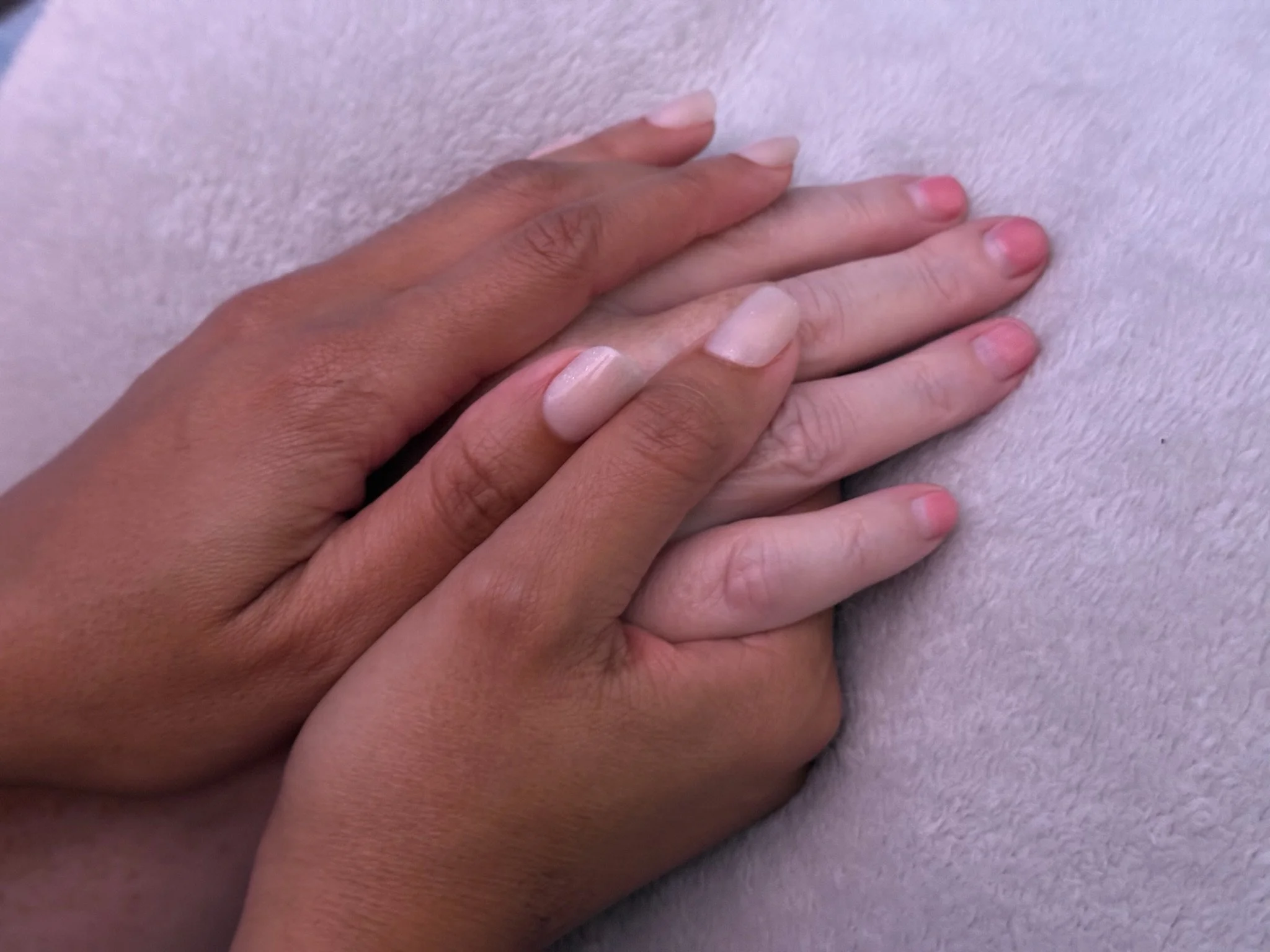 Close-up of two hands with different skin tones gently touching on a soft, light purple surface.