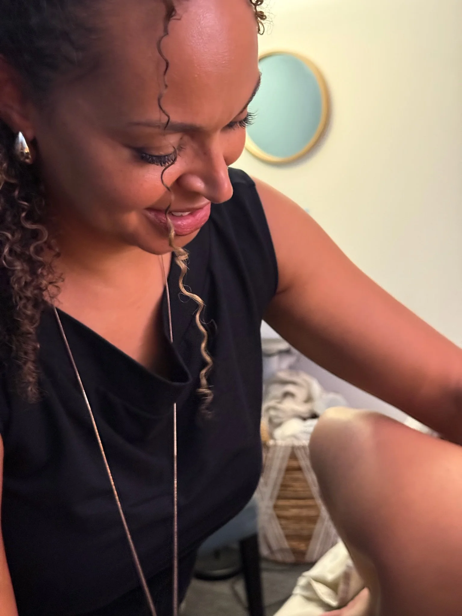 Close-up of Dr. Ihotu Ali wearing a black top, smiling while looking down at her client, in a room with a mirror on the wall.