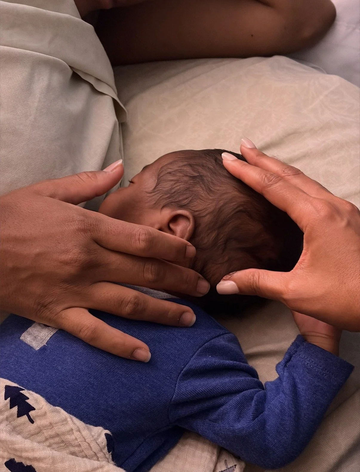 Close-up of a newborn baby lying on a person's lap, gently cradled and receiving their first craniosacral treatment by Dr. Ihotu Ali.