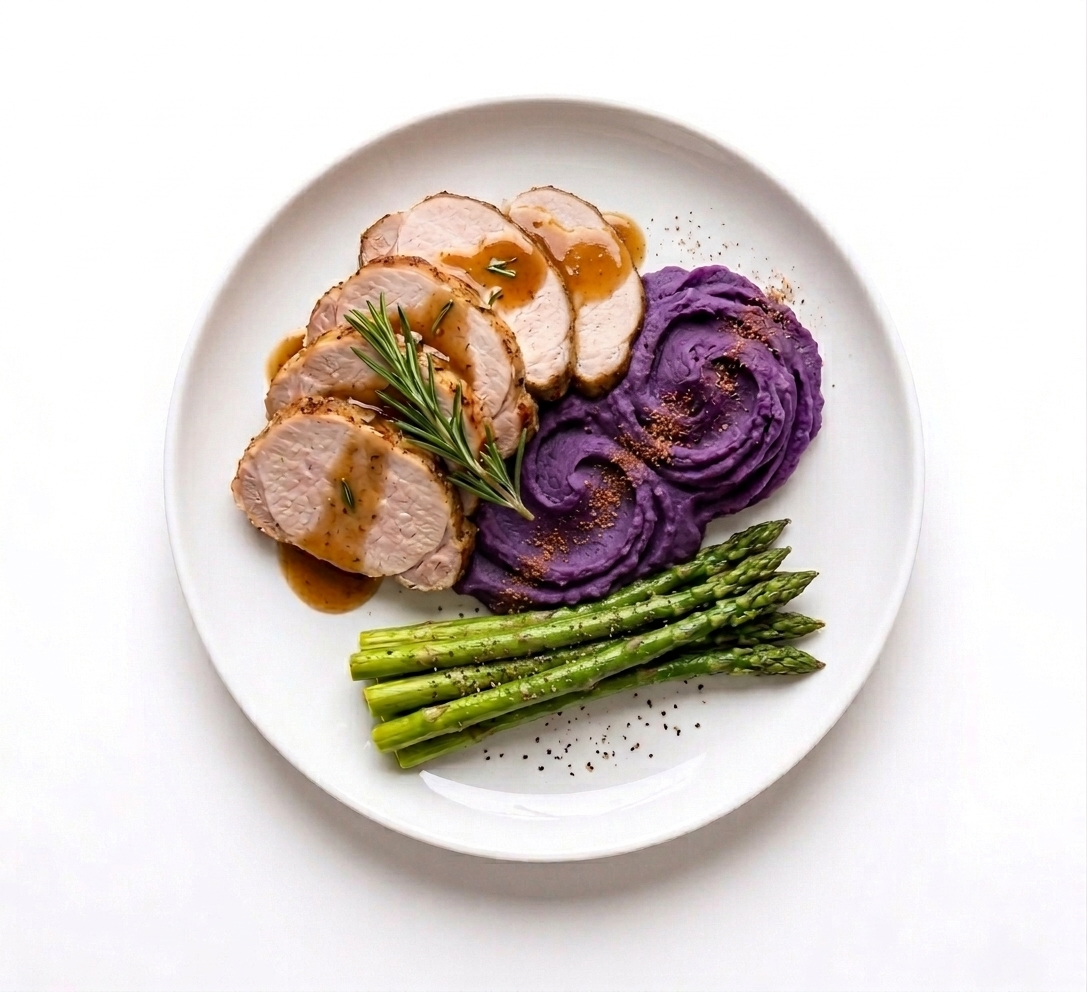 Slices of cooked turkey breast topped with gravy, purple mashed potatoes garnished with seasoning, and a bundle of cooked asparagus with seasoning on a white plate.