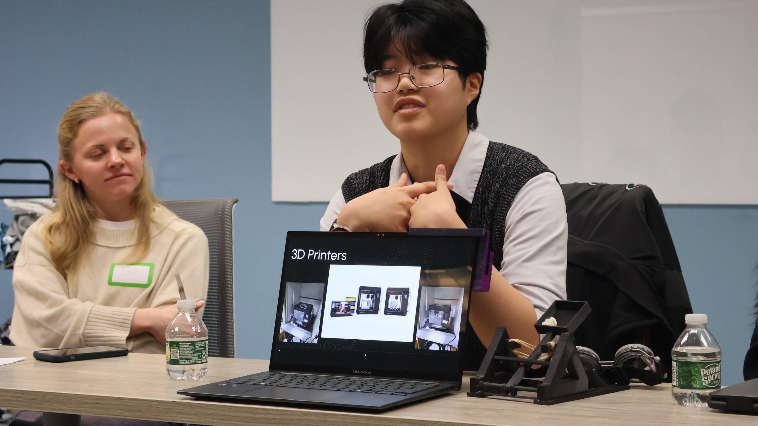 Student sitting behind a laptop showing a 3D printer