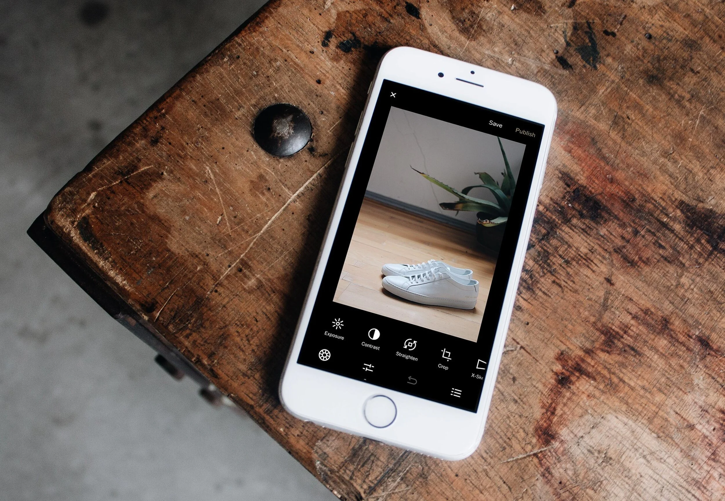 Smartphone on a wooden table displaying a photo of white sneakers and a plant in a black pot.
