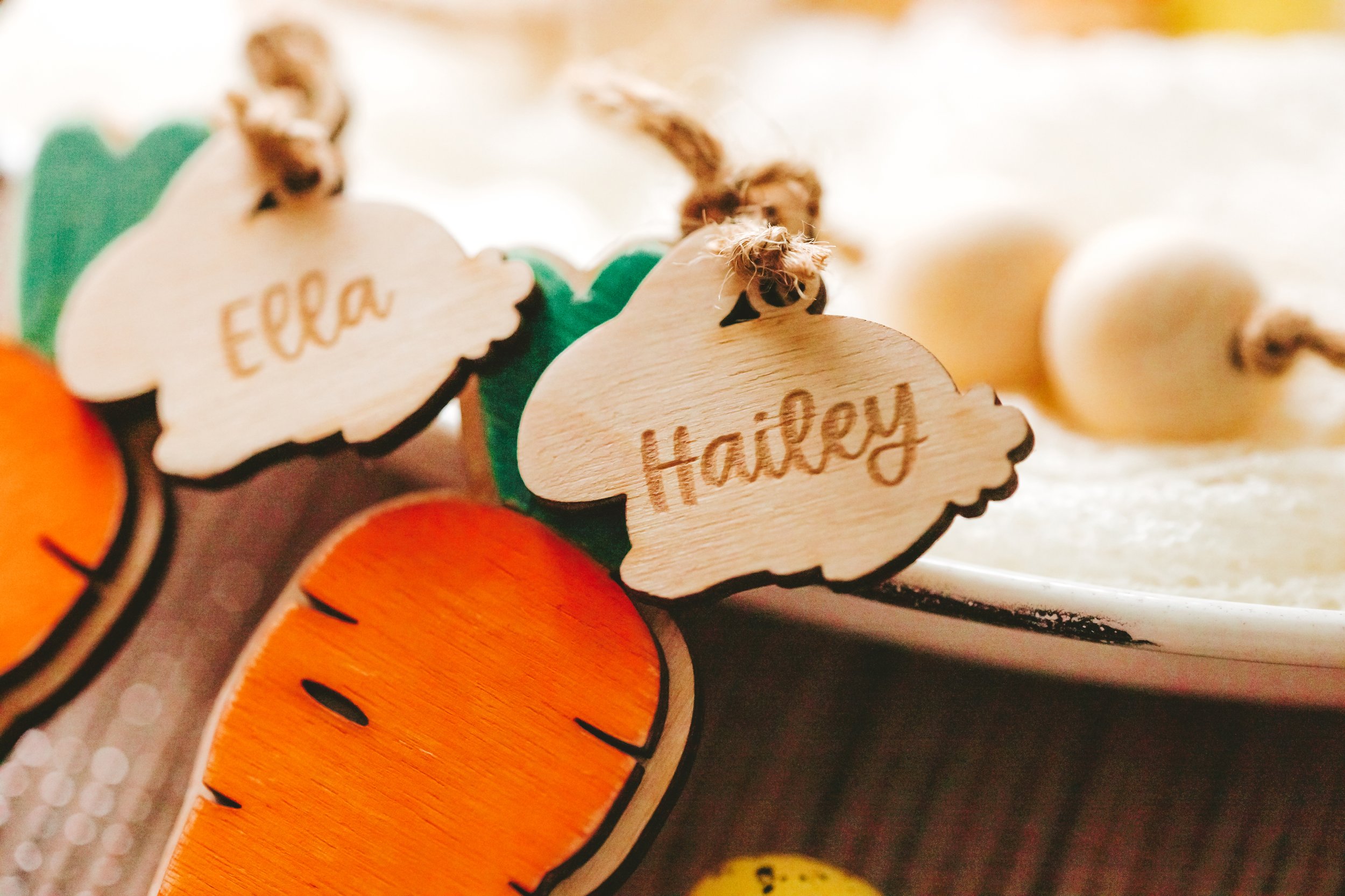 Close-up of wooden pumpkin and cloud-shaped tags with the names Ella and Hailey, part of fall or Halloween decorations.