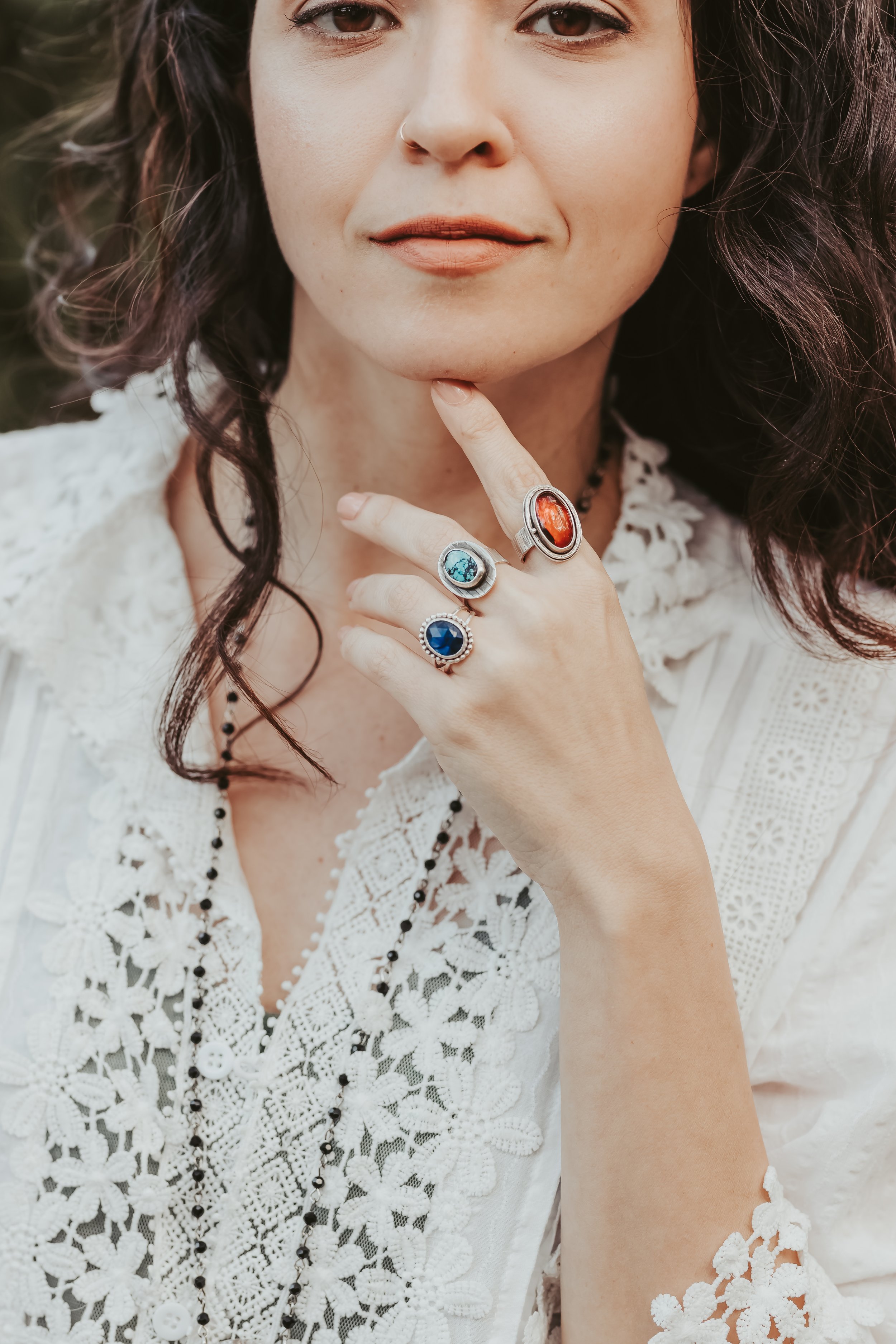 hand model with handmade gemstone rings on three fingers with hand positioned under chin