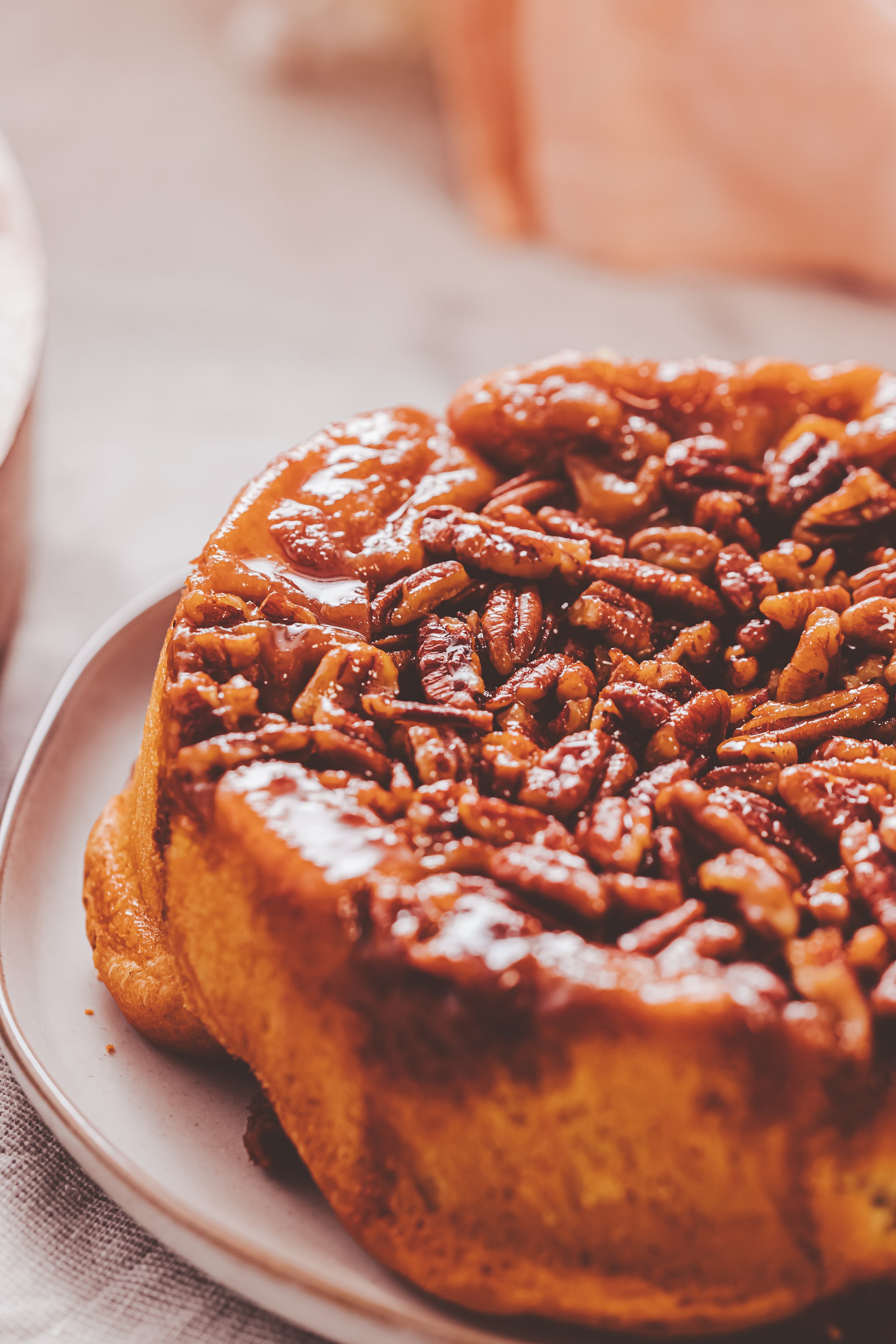 Close-up of a pecan pie on a white plate, showing a golden crust filled with glossy, caramelized pecans.