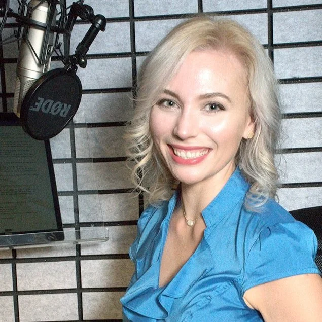 Smiling woman in blue shirt near microphone and audio recording equipment.