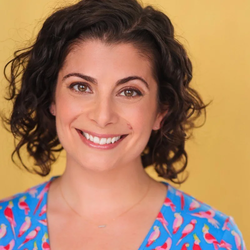 Person smiling, wearing a blue shirt with colorful bird patterns, against a yellow background.