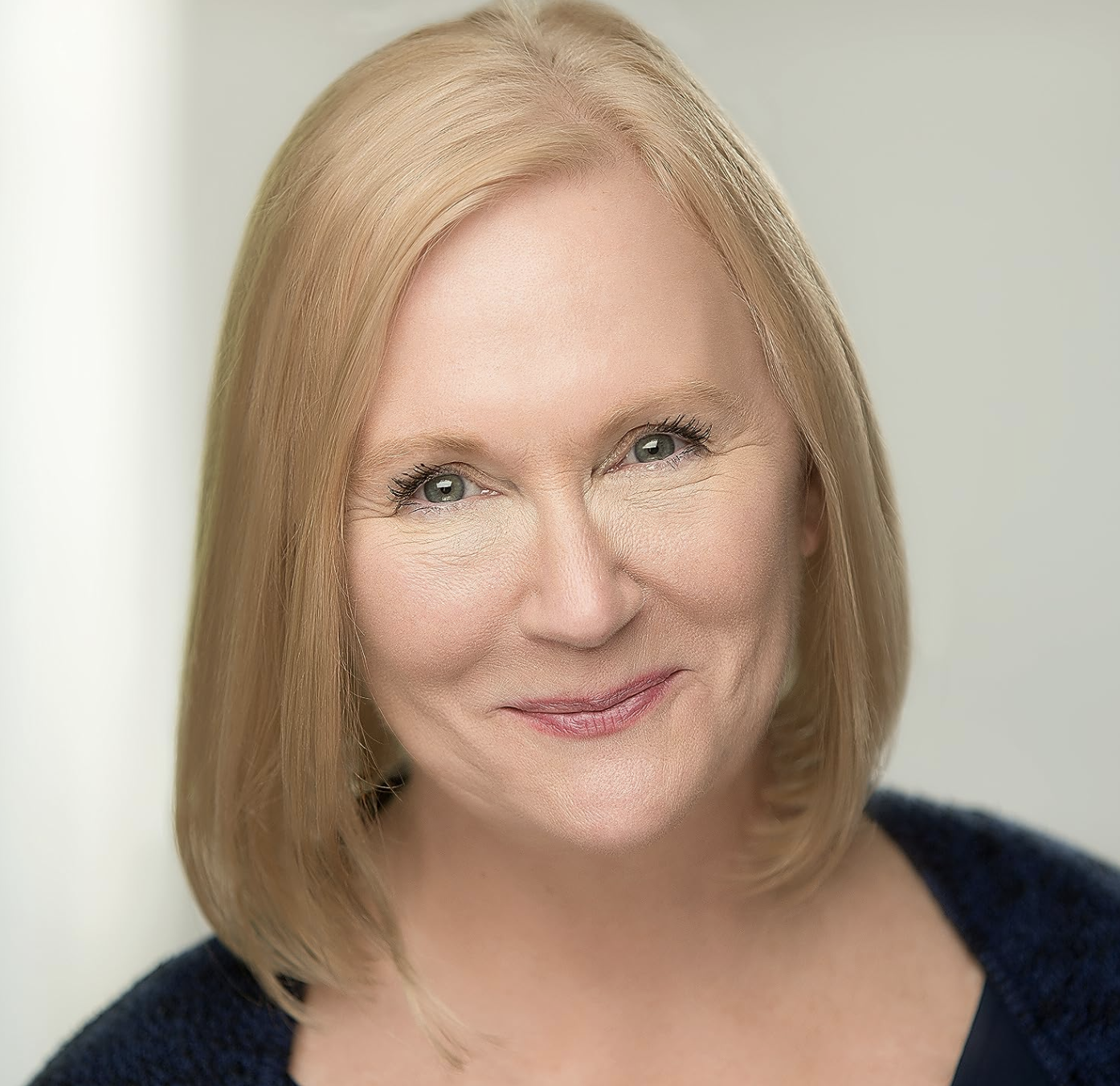 Smiling woman with blonde hair in a close-up portrait, wearing a dark top.