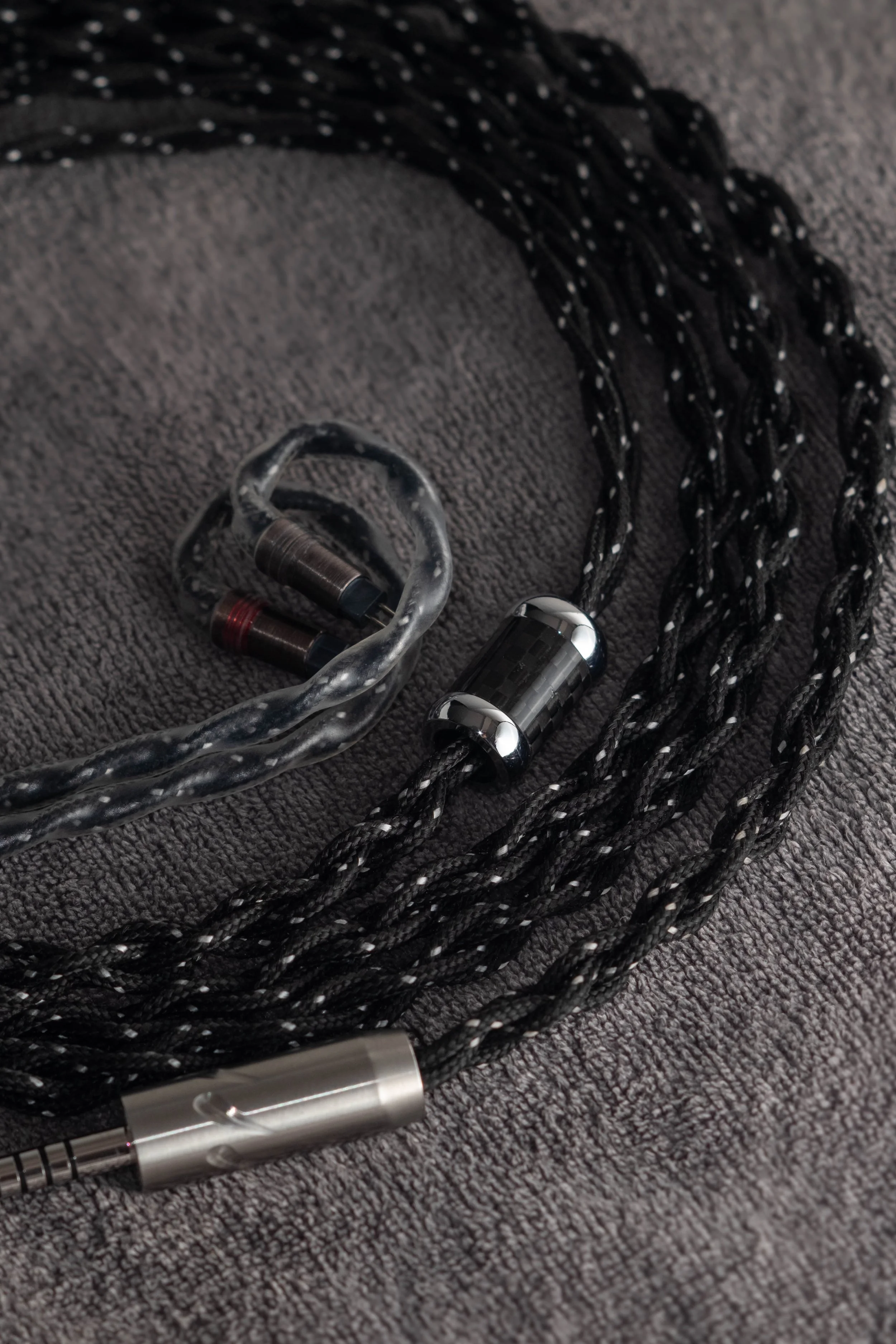 A pair of custom in-ear monitors, with a braided black and white cable, and a 3.5mm audio jack, placed on a gray fabric surface.