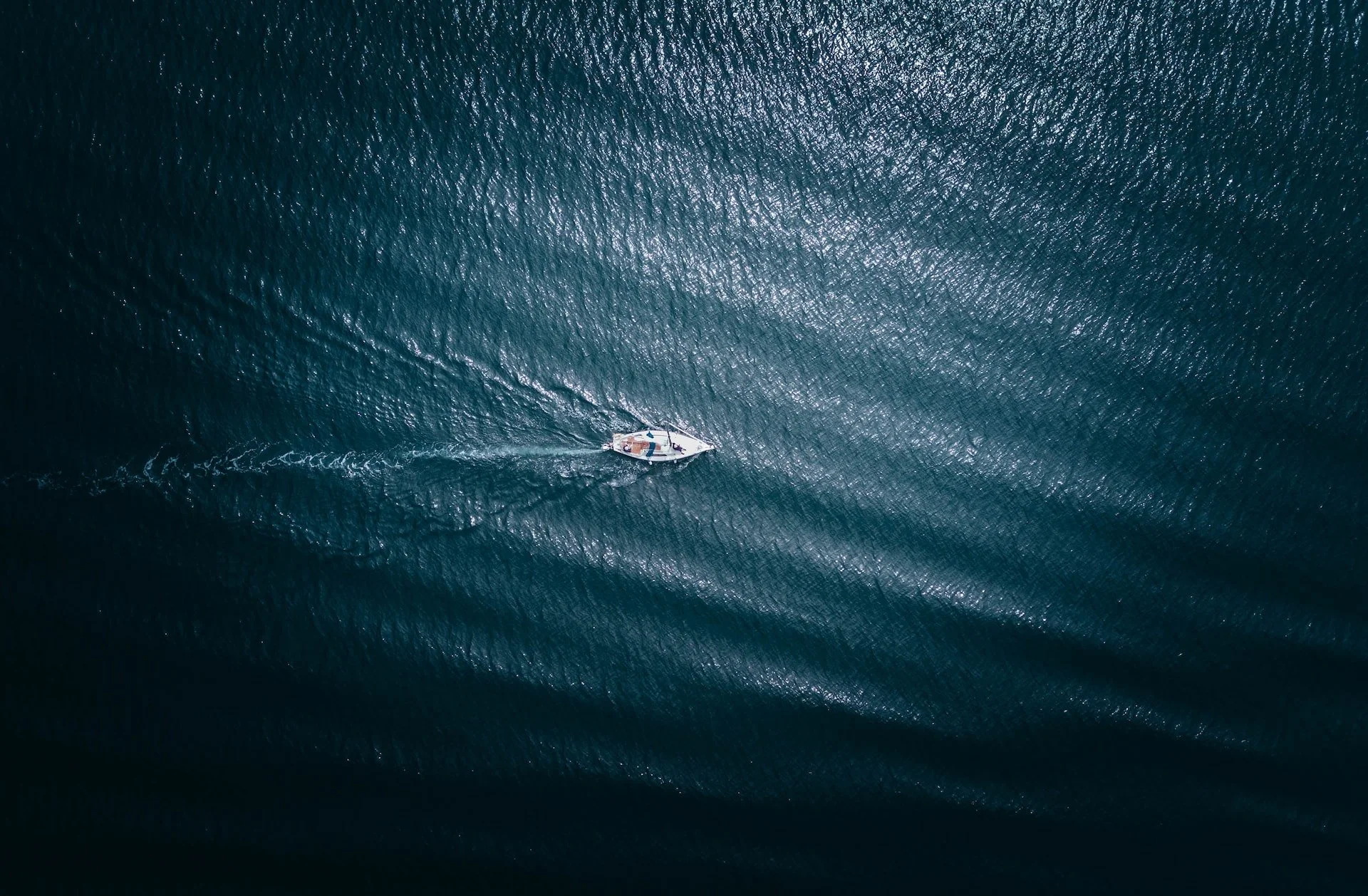A view from the sky looking down on a sailboat crossing an open sea. The boat looks small and vulnerable.