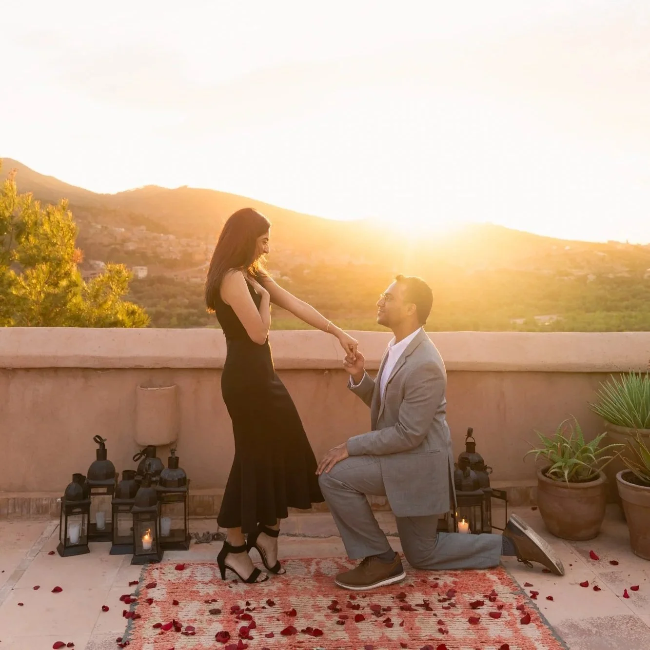 A man proposing marriage to a woman in a scenic garden with mountains in the background.