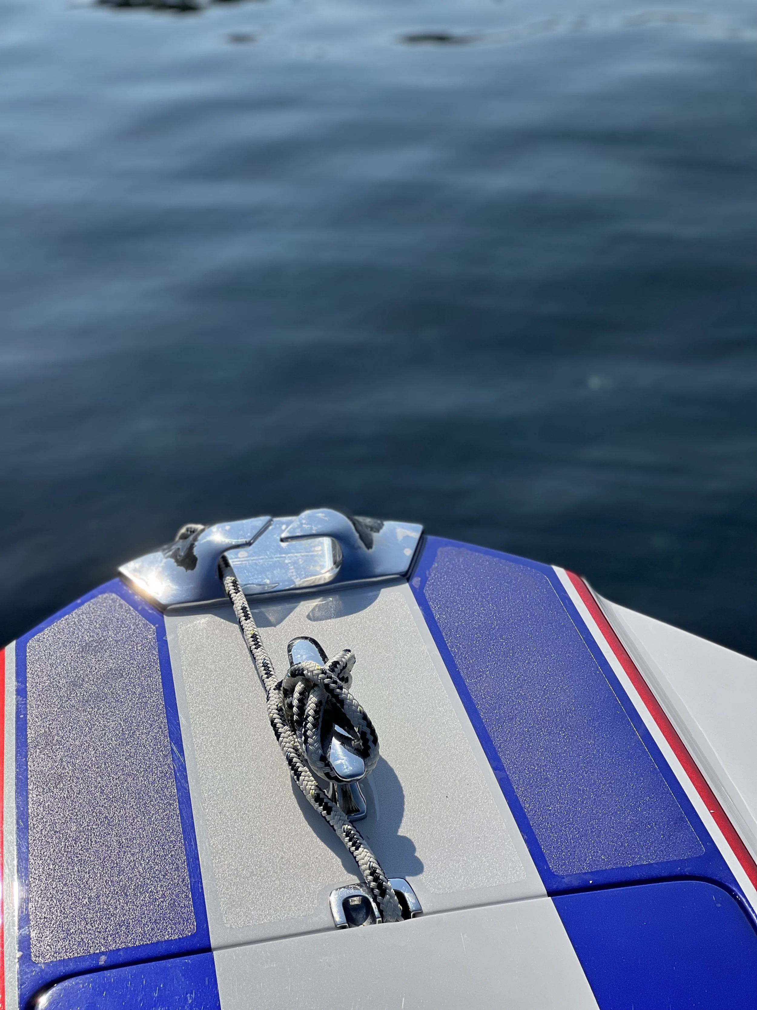 Close-up of a boat's bow with a metal cleat and a coiled rope, on calm open water.