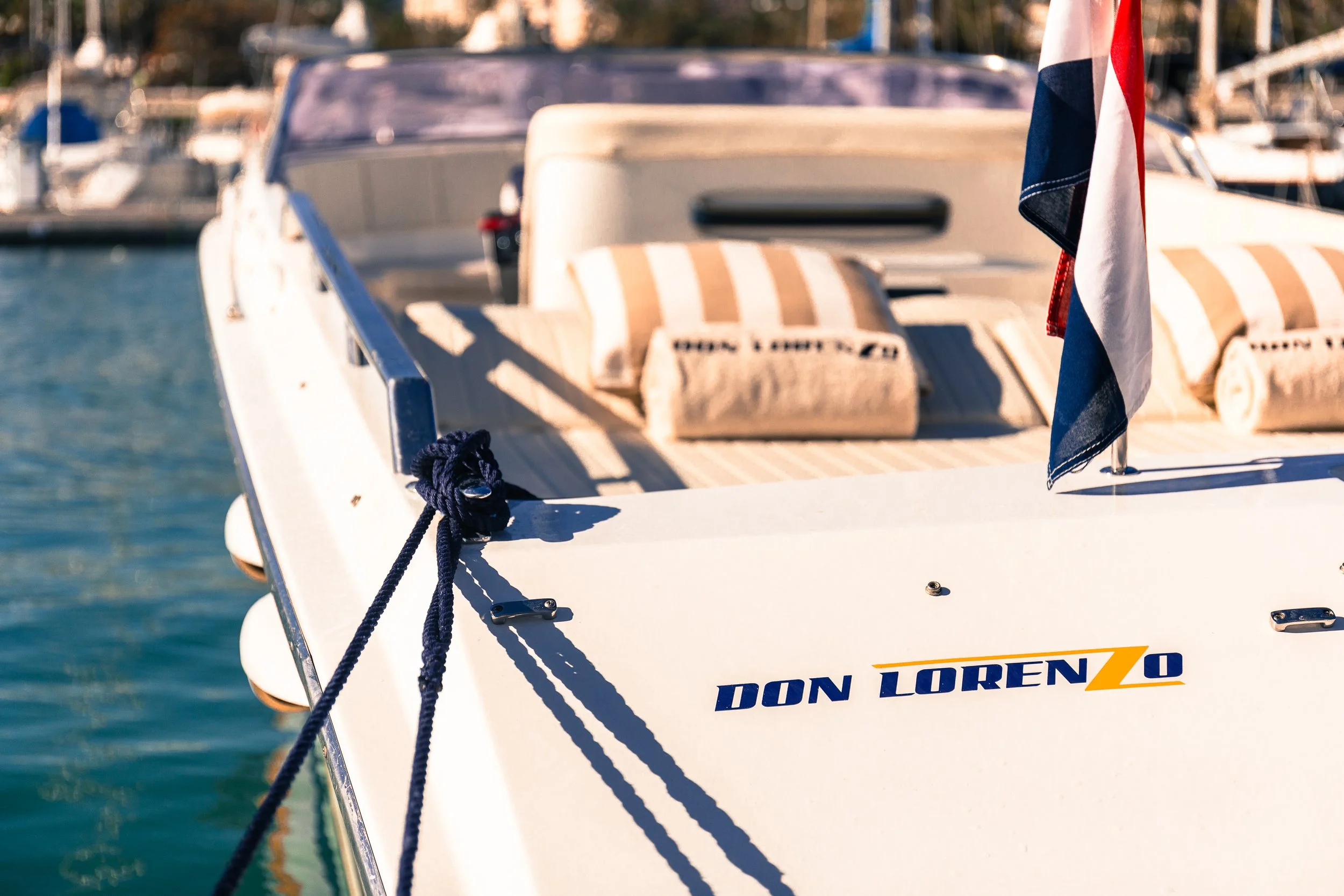 Close-up of a white yacht named 'Don Lorenzo' docked at a marina with striped cushions on deck and American flag.