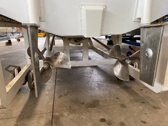 View of boat's metal propellers and drive system underneath in a warehouse or hangar.