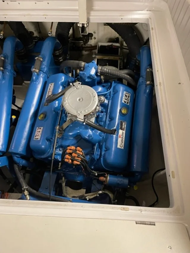 Blue boat engine with visible hoses and components inside a white fiberglass compartment.