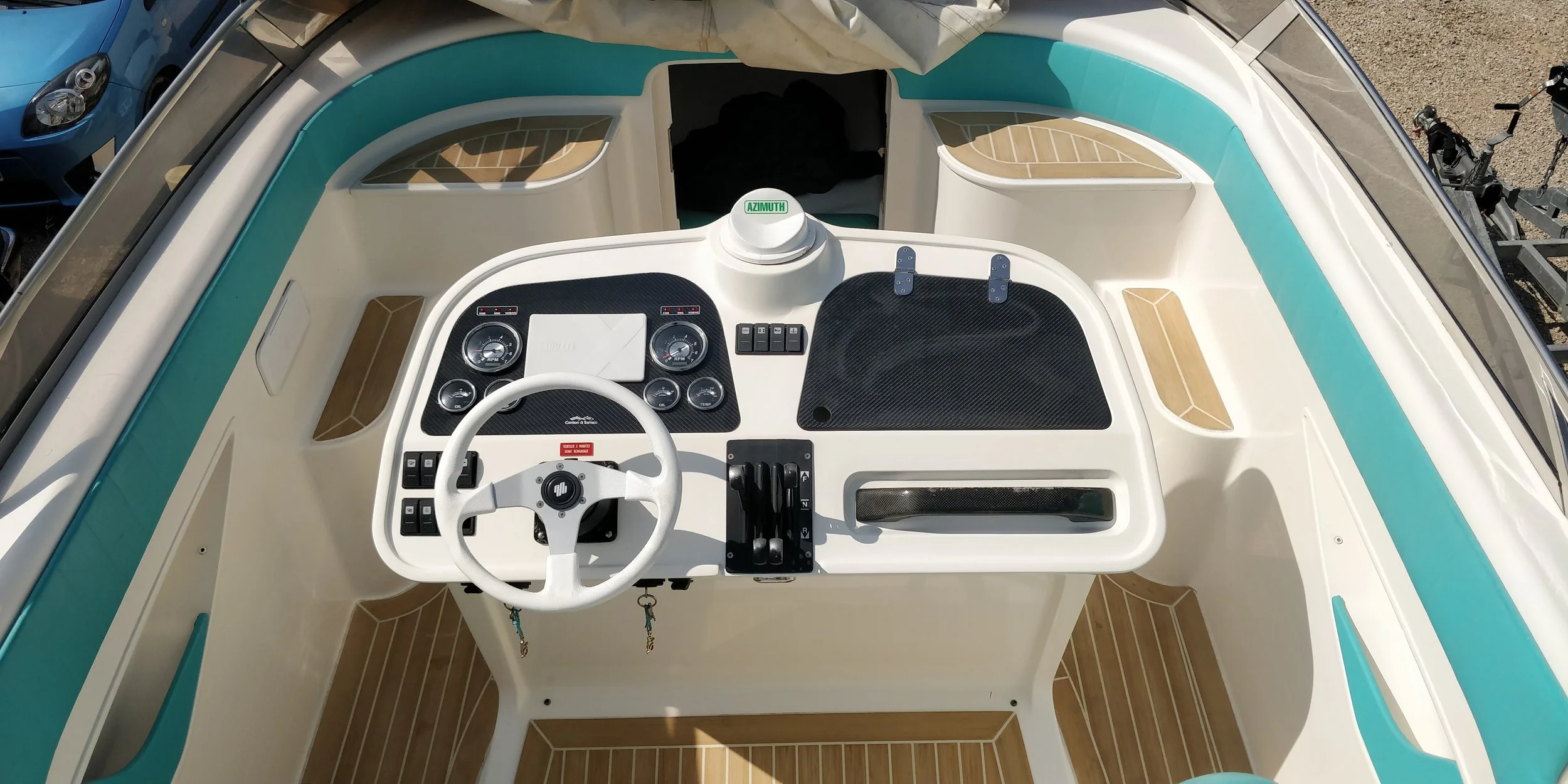The cockpit of a small motorboat with a white steering wheel, control panels, and gauges, with blue and brown accents, and a dashboard labeled AZIMUTH.