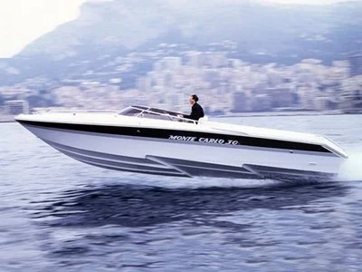 A person driving a speedboat on the water with a city skyline and mountains in the background.