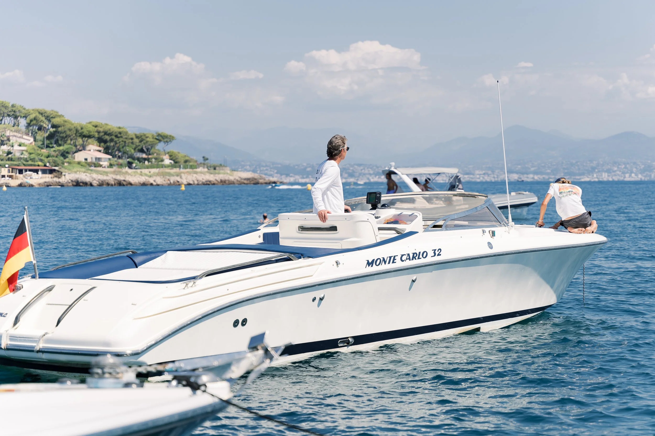 People on a white yacht named Monte Carlo 32 on the water with a scenic background of hills and sky.