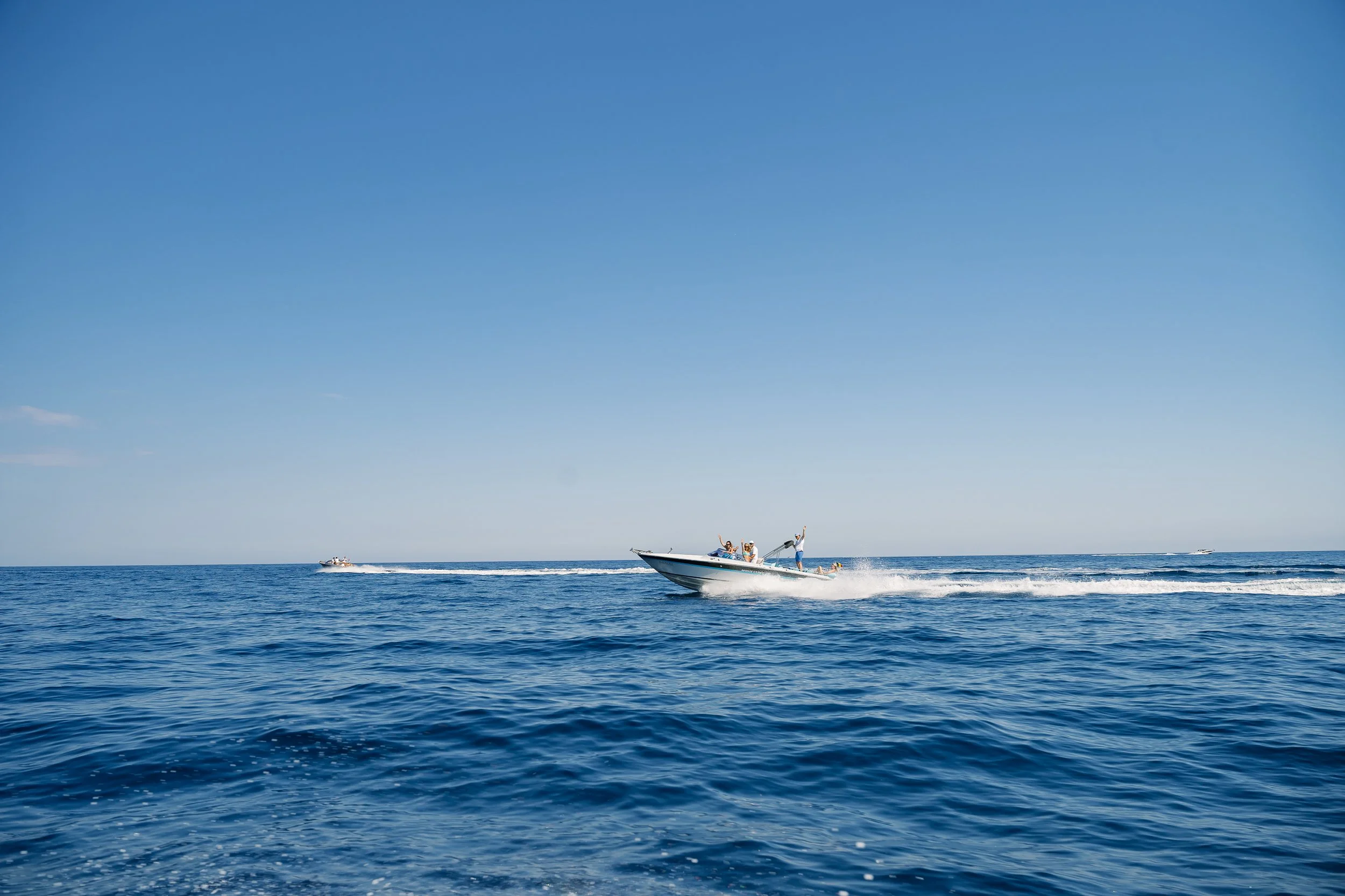 People enjoying a boat ride on the ocean on a sunny day, with clear blue sky and calm waves.