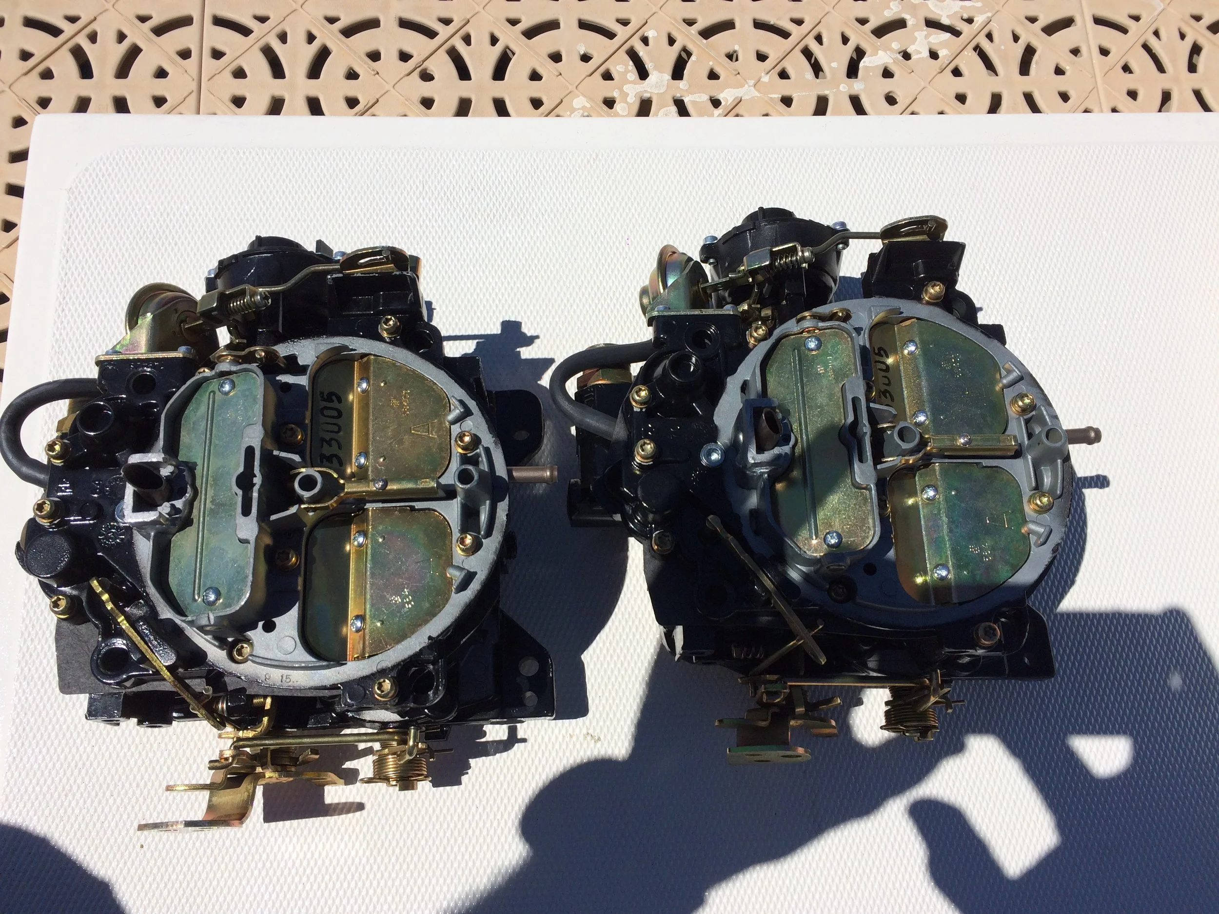 Two carburetors placed side by side on a white surface with a brown patterned background.
