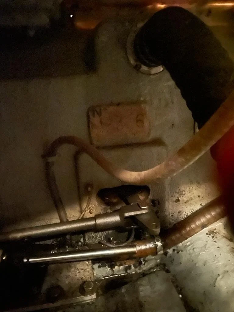 Close-up of mechanical parts including pipes, a joint, and a rusty plate in a dark, confined space.