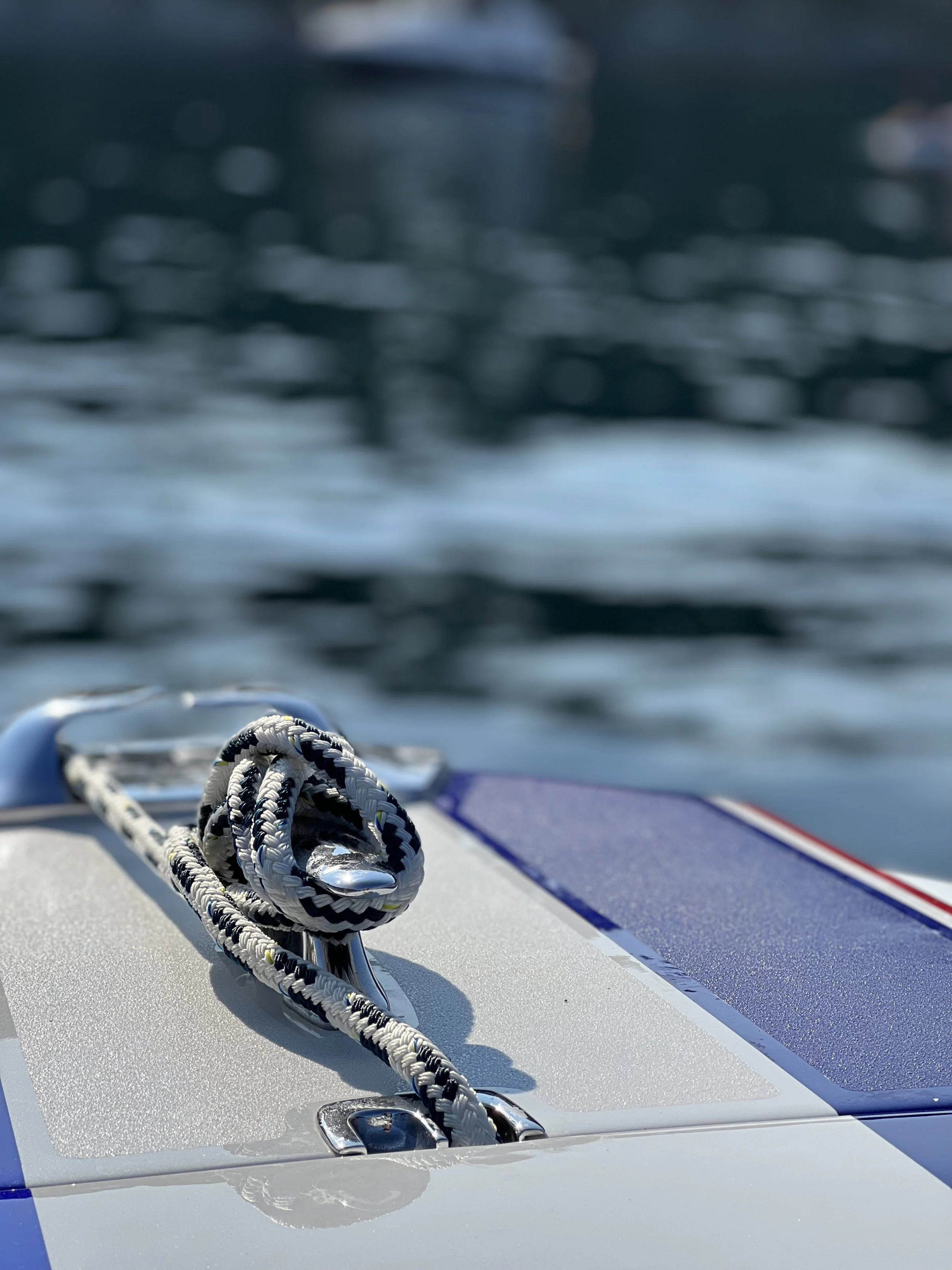 Close-up of a coiled rope and metal cleat on a boat deck with water in the background.