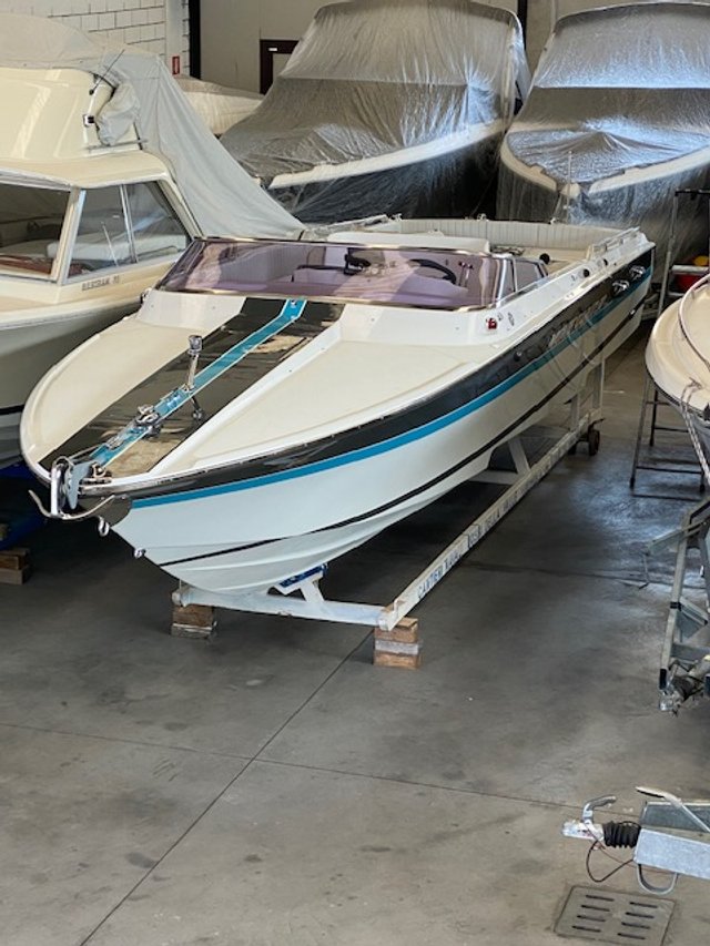 A motorboat on a wooden stand inside a storage garage, with other boats covered with protective sheets in the background.