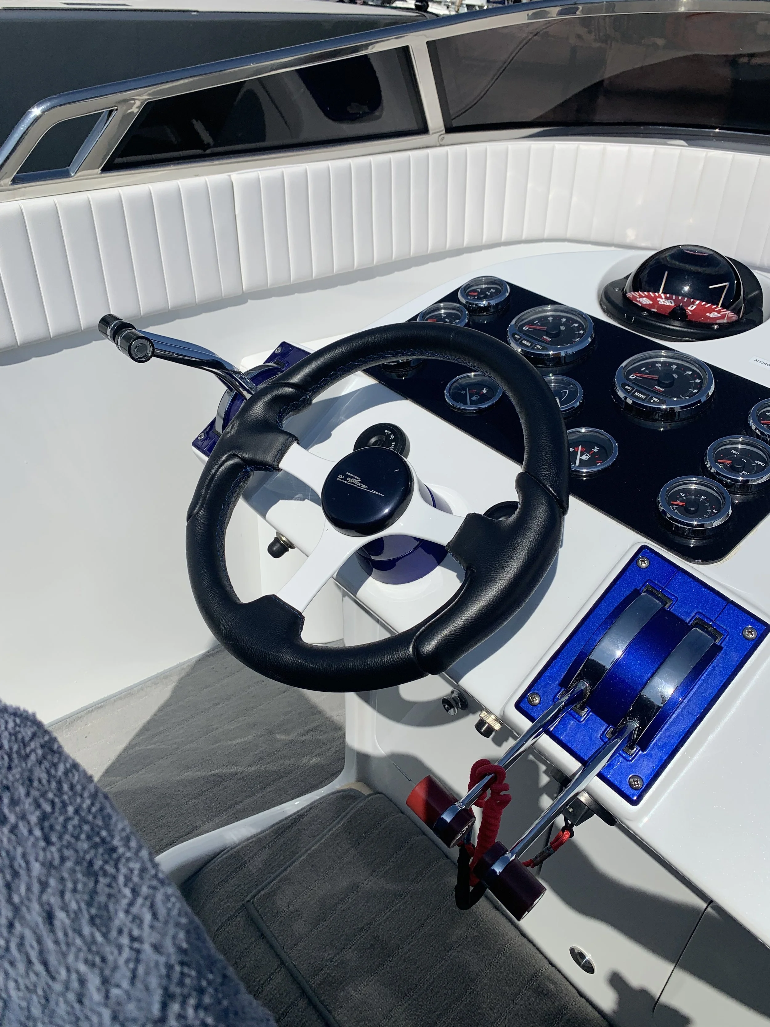 Close-up of a boat's dashboard with multiple gauges, a steering wheel, and a throttle control with a red lanyard, set against white weathered surfaces.