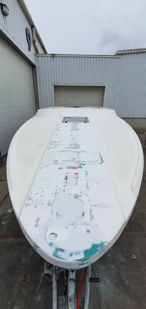 A boat on a trailer outside a building with white walls and a closed garage door, showing the boat's top surface with peeling paint.