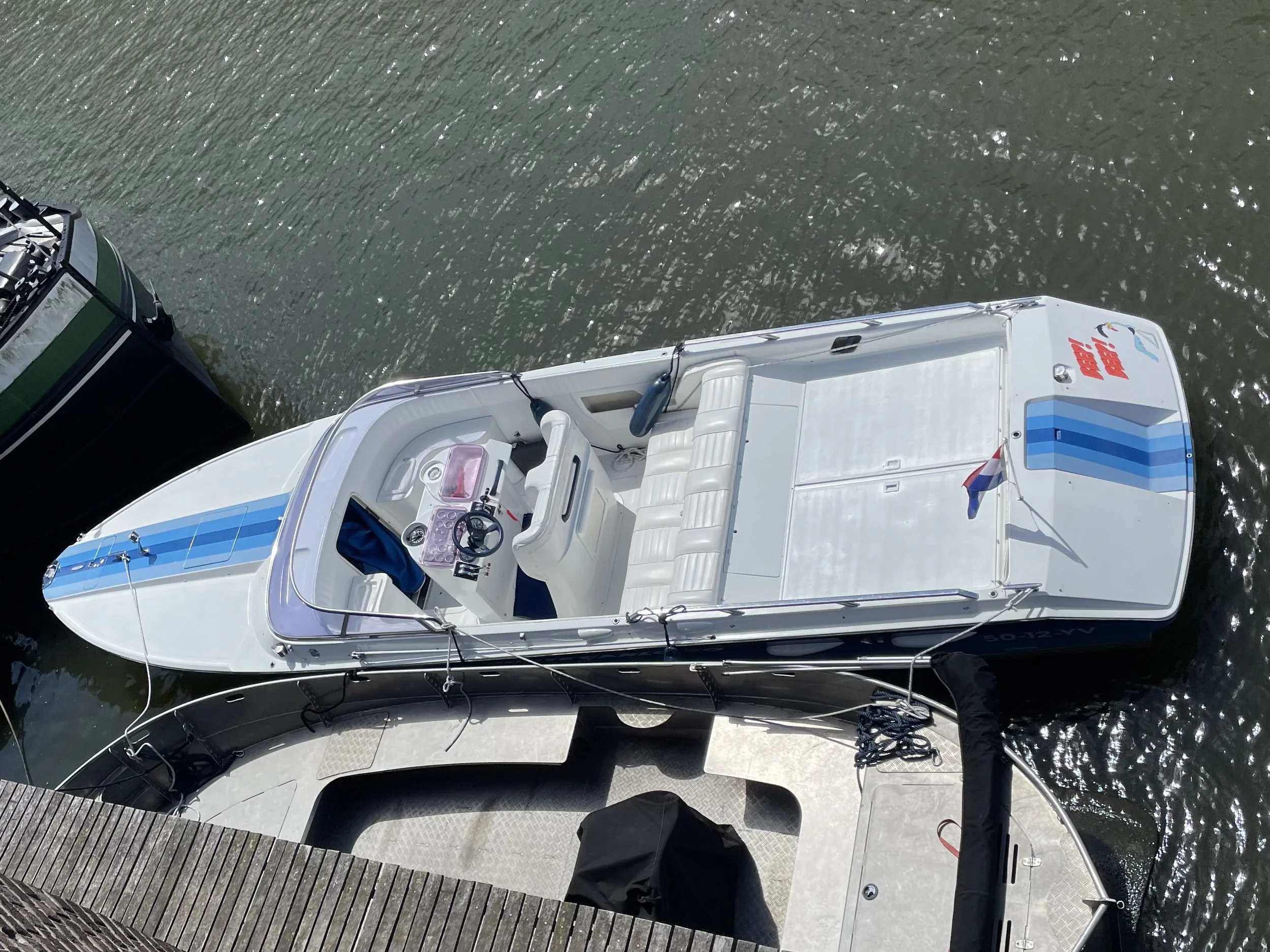 An aerial view of a white boat docked at a marina, with a black boat nearby and a dock at the bottom.