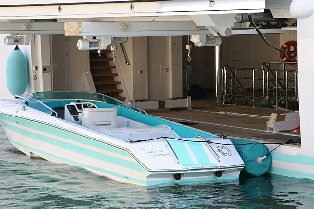 A speedboat docked next to a large white boat with a ramp or platform.