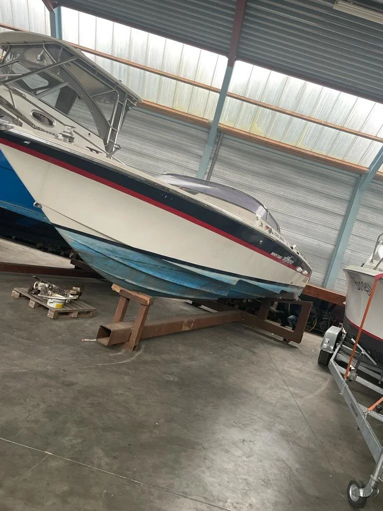 A motorboat with a white, black, and red design stored on a wooden stand inside a warehouse or garage, with another boat partially visible on the right.