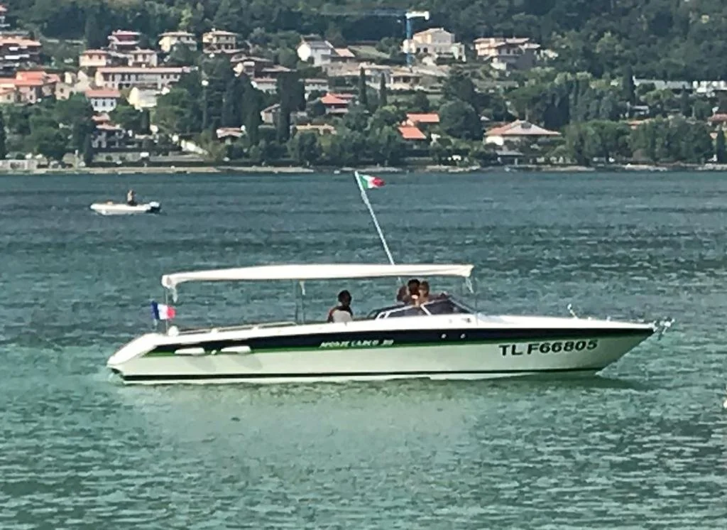 A motorboat with passengers on a lake, with a small motorboat in the background and a hillside residential area.