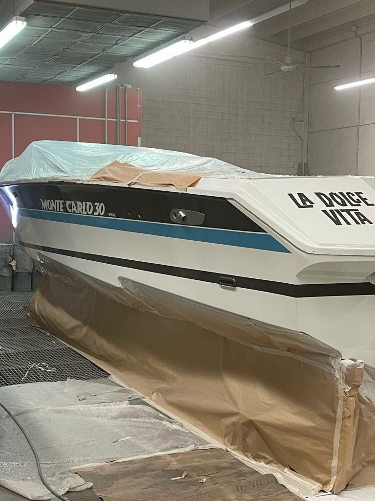 A boat on a stand in a warehouse, partially covered with plastic and paper for protection or painting.