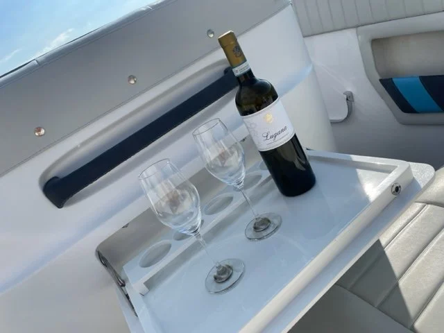 A bottle of red wine and two empty wine glasses on a white tray inside a boat or yacht