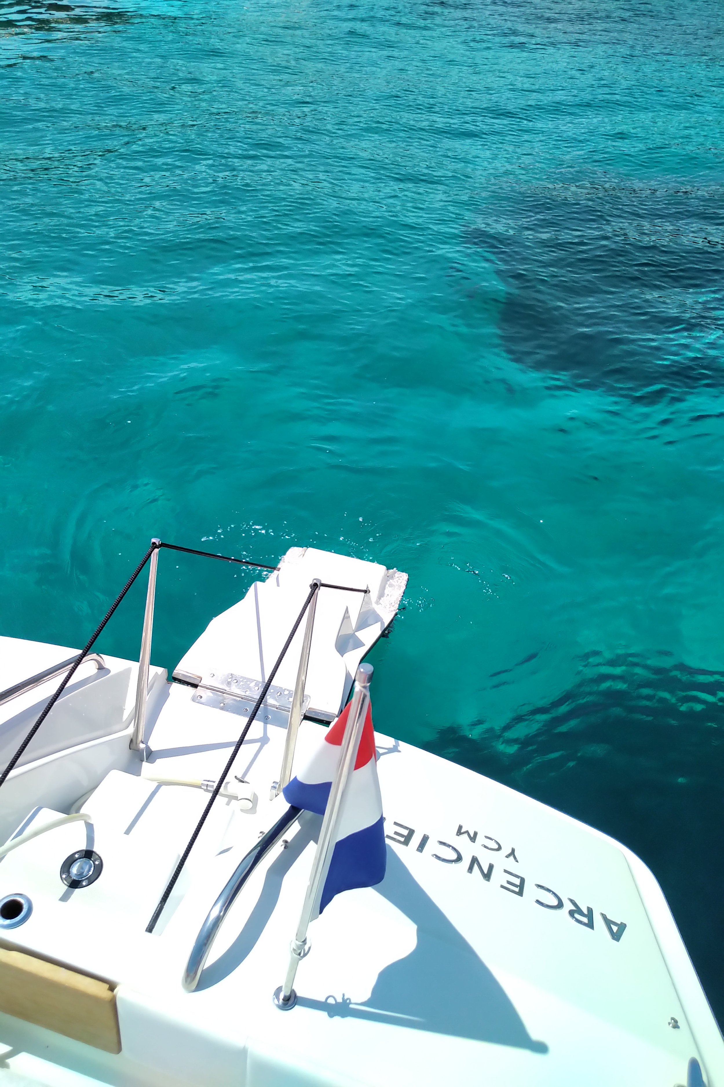 A boat named 'Arrecife WC' floating on clear blue water, with a small French flag near the bow.