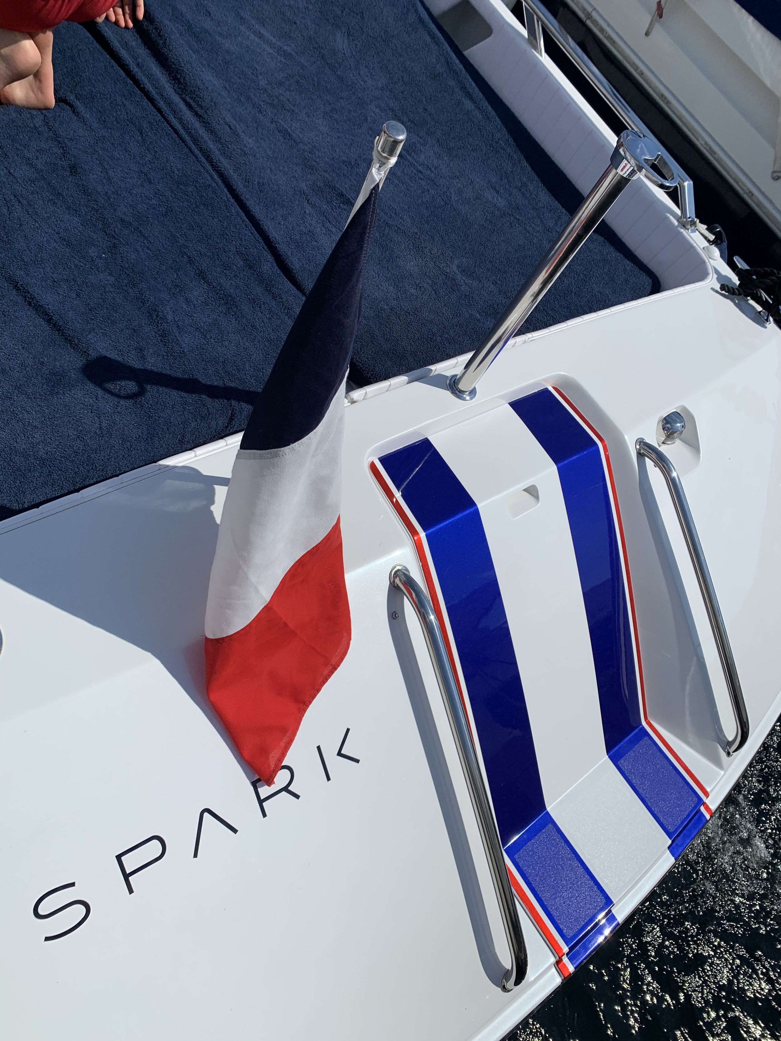 Close-up of a sailboat with a nautical flag attached to it, featuring bold blue, white, and red stripes, with the word 'SPARK' written on the hull.