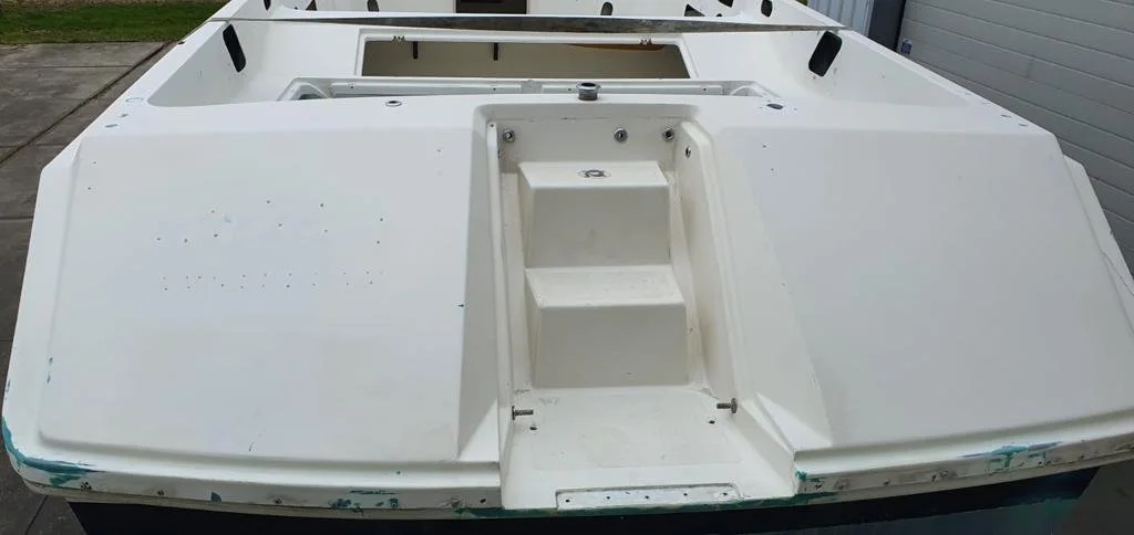 White boat deck with steps in the center, some chipped paint at the edges, and an open hatch at the back.
