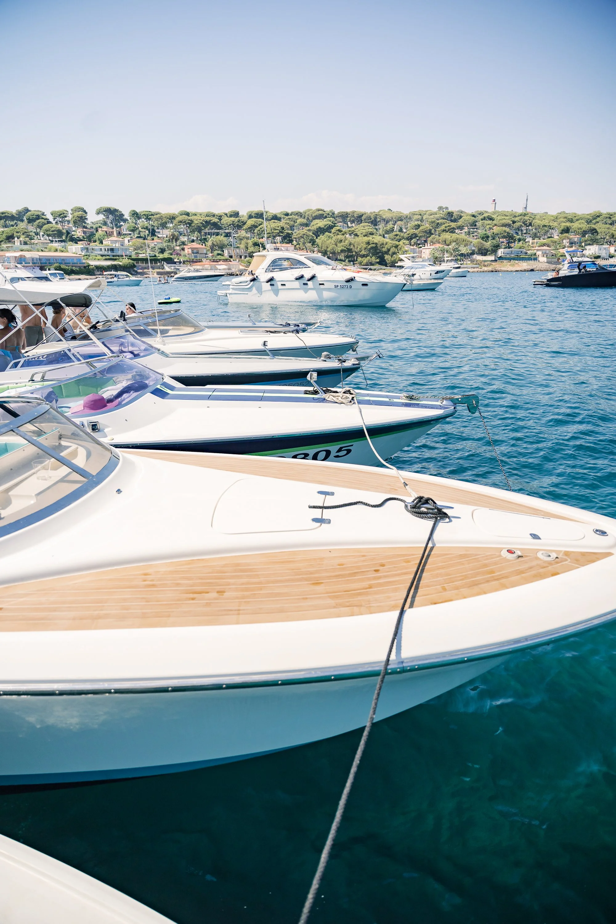 Numerous boats docked at a marina on a sunny day with a hilly background and a clear blue sky.