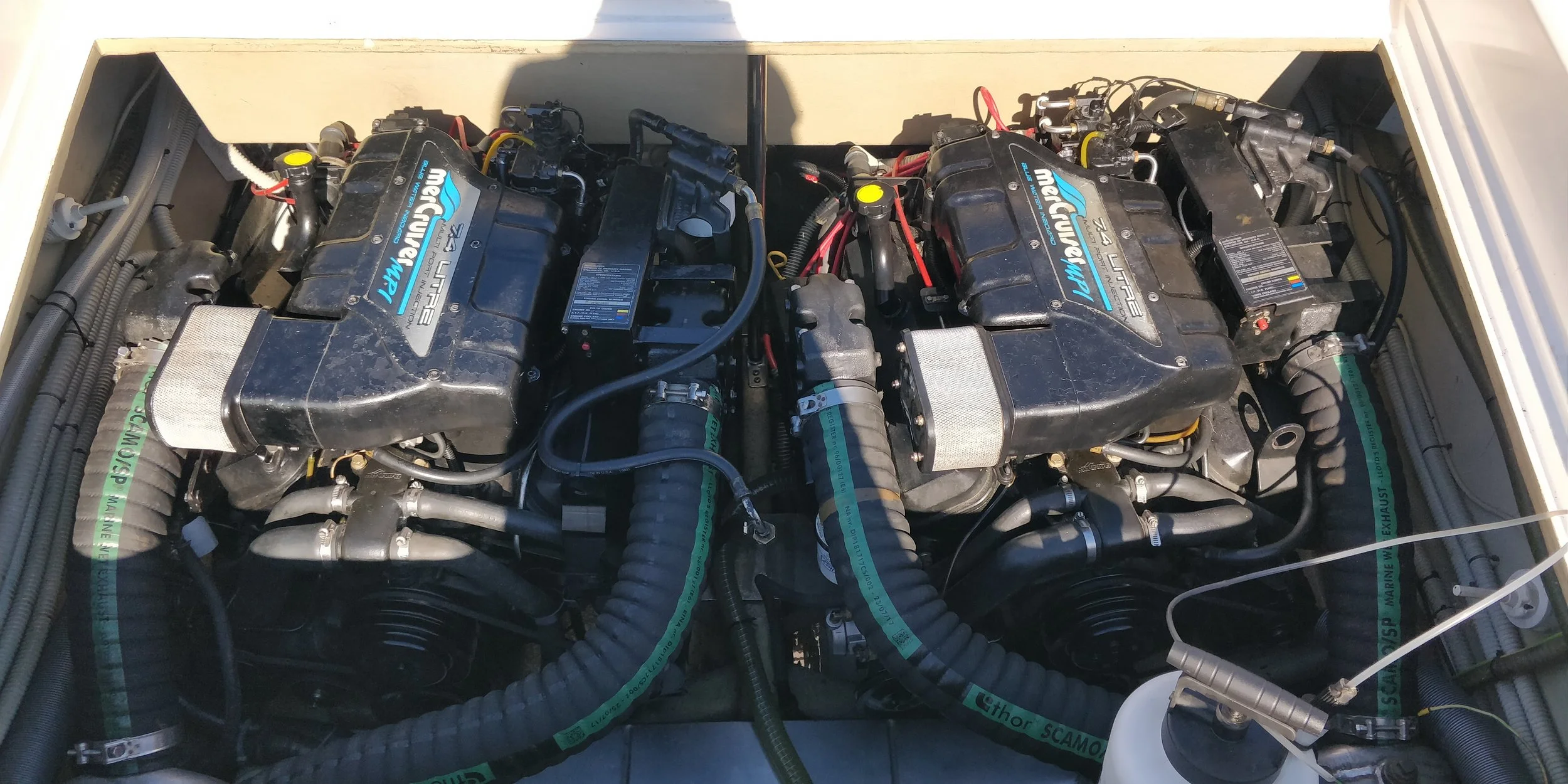 Dual MerCruiser 7.4L Litre large marine engines with black covers, hoses, and electrical connections inside boat engine compartment.