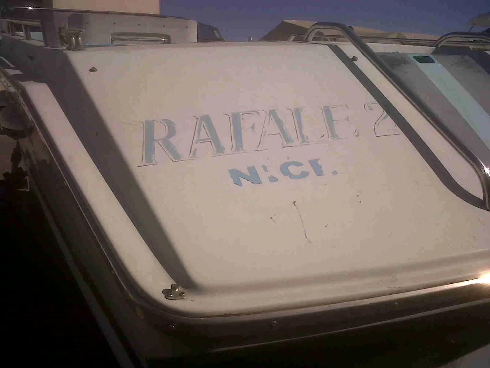 Close-up of a car roof with a faded sign that reads "RAFALF N.C." in blue letters, surrounded by other vehicles in a parking lot, under daytime sunlight.