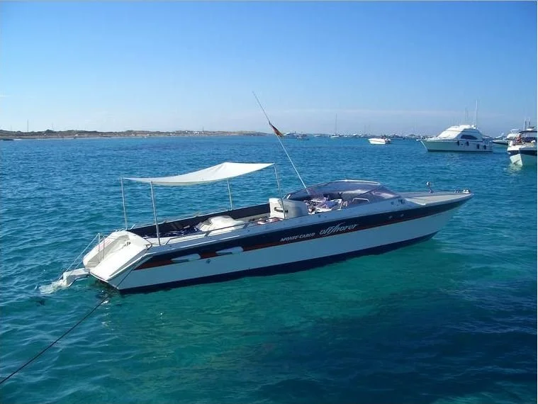 A white and black motor yacht with a canopy, anchoring in a harbor with other boats, and clear blue water under a sunny sky.