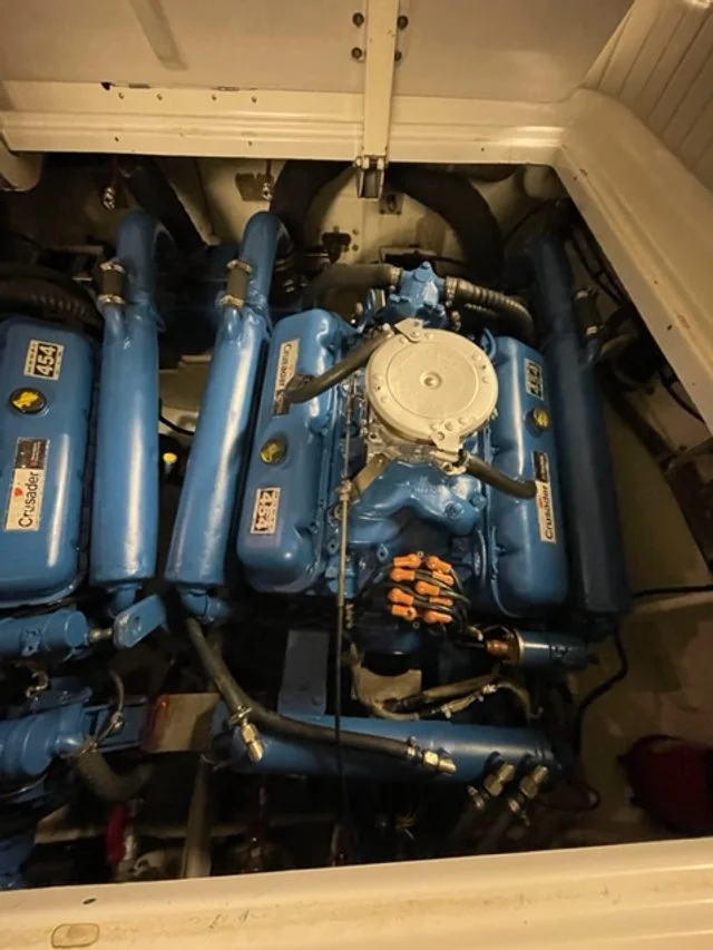 The image shows a blue marine engine with various labeled components and hoses, installed inside a boat engine compartment.