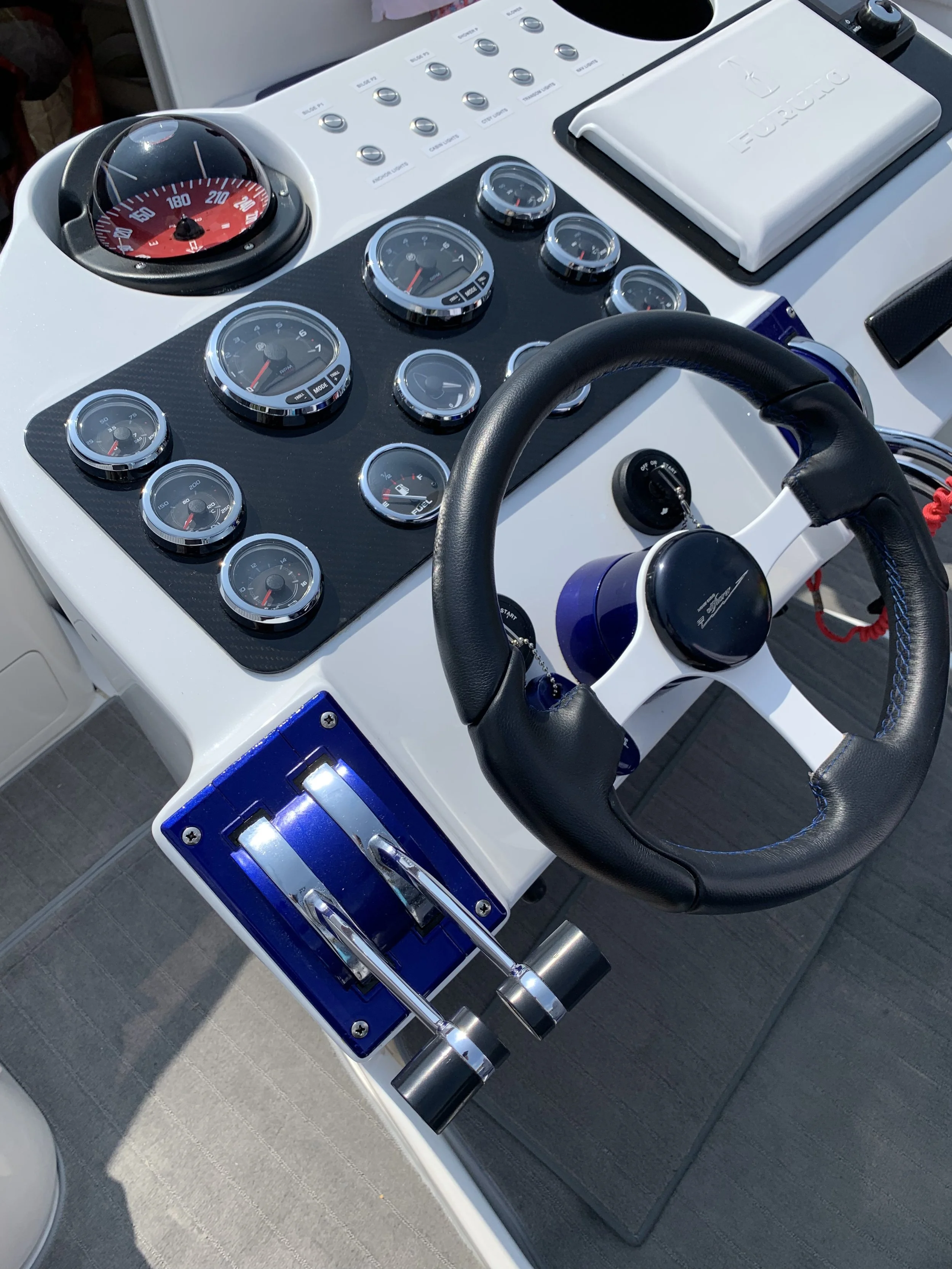 Boat control console with multiple gauges, a throttle, a steering wheel, and marine electronics.