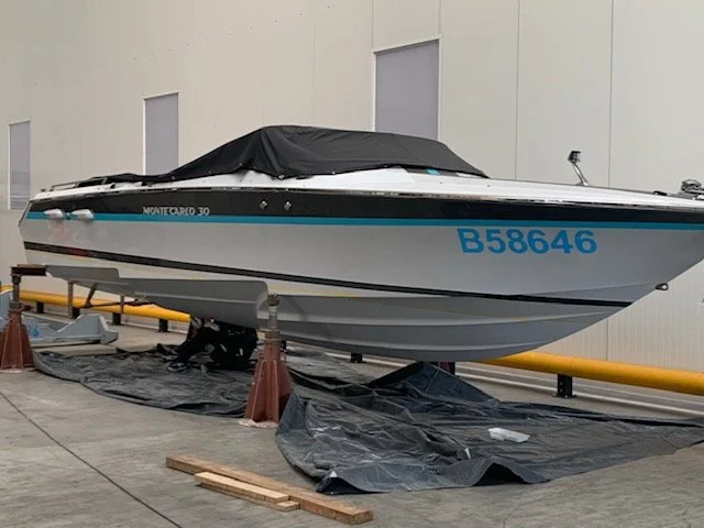 A motorboat named 'Montgomery 30' stored indoors on supports with a black cover over part of it, known as a speedboat with a blue registration number 'B58646'.