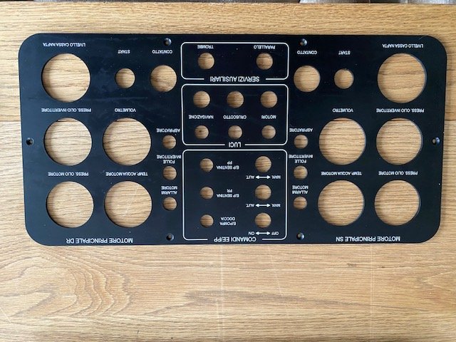 Black metal tool with various circular and rectangular cutouts, labeled with terms related to audio and video equipment, resting on a wooden surface.